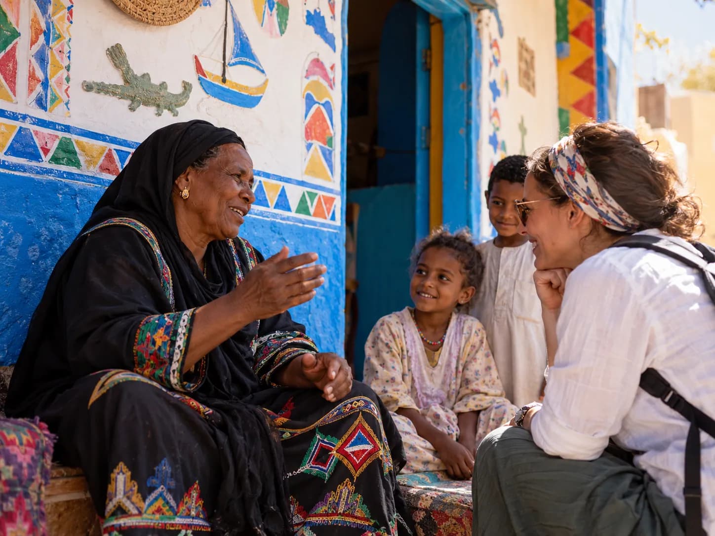 A Nubian woman chatting with a family in front of a painted blue wall